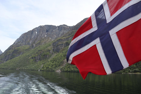 Red with a blue Scandinavian cross in a white border Flag of Norway in the wind over the water of the fjordの写真素材