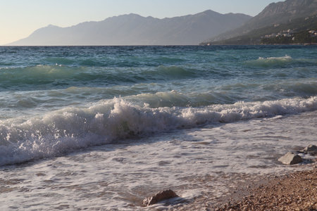Waves on a pebble beach, mountains on the horizon on a summer dayの写真素材