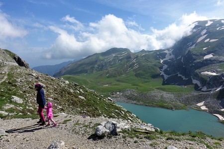 Family hiking. Mother and daughter move on a hiking path towards Kseroloutsa / Laka Tsoumani. Below them is an alpine glacier lake is visible. Opposite an astonishing view of green slopes with snow patches reveals it self.の写真素材
