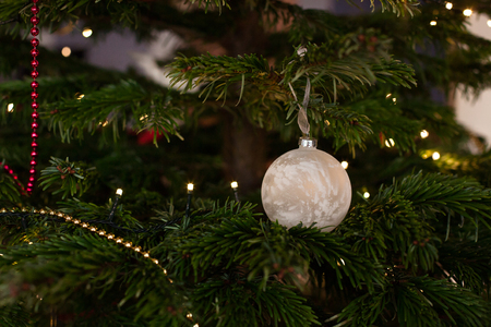 Closeup of red bauble hanging from a decorated Christmas tree.の写真素材