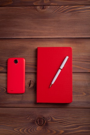 Red notebook and a smartphone on a dark wooden background. In search of ideas.