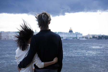 Back view of man and woman huging together on the bridge on the background of the river.の写真素材