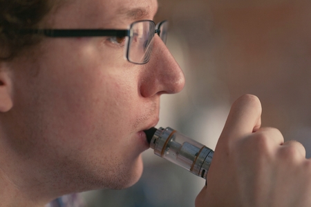 Young man smoking electronic cigarette near window. vaping.の写真素材