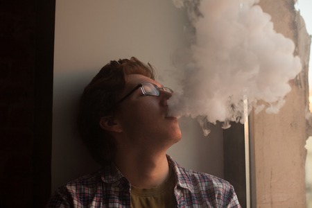 Young man smoking electronic cigarette near window. vaping.の写真素材