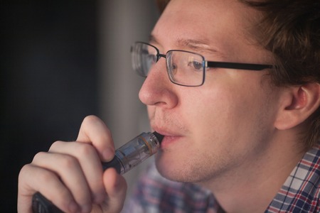 Young man smoking electronic cigarette near window. vaping.の写真素材