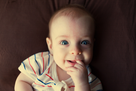 Portrait of a little blue-eyed boy, who lies on a bed and put her finger in her mouth.の写真素材