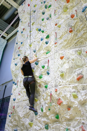 Young athletic woman practicing rock-climbing on a rock wall indoors.の写真素材