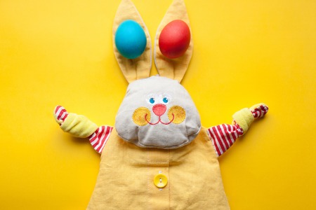 Easter decorations from a handmade toy rabbit and colorful eggs on an orange background.の写真素材