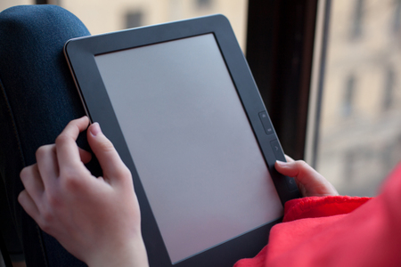 A woman sits by the window and uses an e-book. blank screen.
