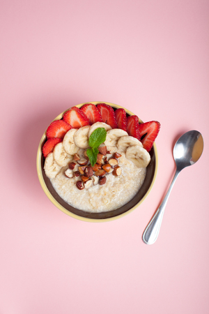 Bowl of oatmeal with a banana, strawberries, almonds, hazelnuts and butter on a pink background. Hot and a healthy dish for Breakfast, top view.の写真素材