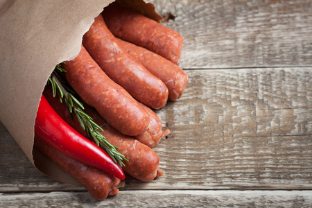 Raw homemade sausages of lamb with rosemary and chili pepper in a paper envelope on wooden tableの写真素材