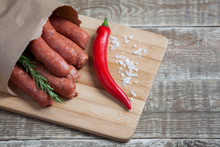 Raw homemade sausages of lamb with rosemary and chili pepper in a paper envelope on wooden table.の写真素材