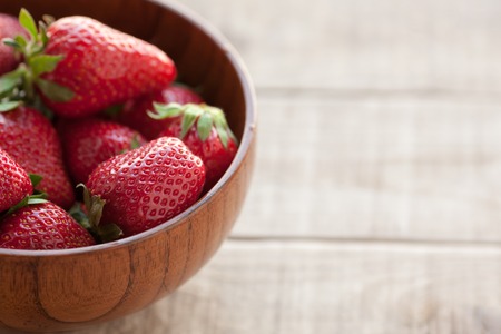 Fresh strawberries in a wooden bowl on a wooden table.の写真素材