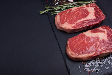 Two fresh raw marble meat, black Angus ribeye steak with spices on a dark stone background. With copy space.の写真素材