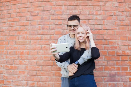 Young couple photographing a selfie with smartphone on the background of red brick wall.