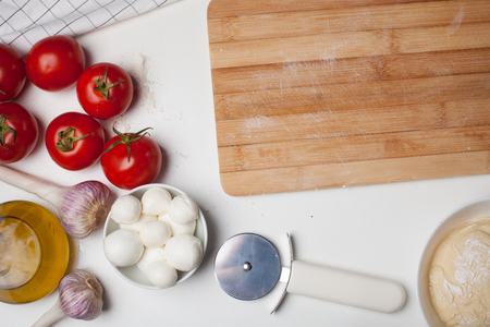 Wooden cutting Board with ingredients for homemade pizza on a white table.の写真素材