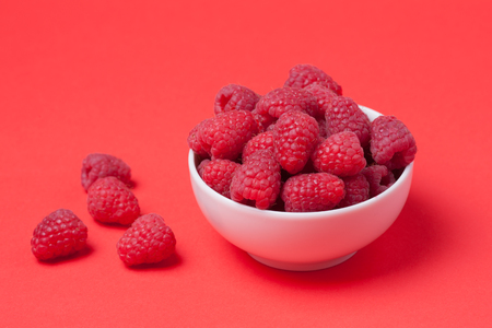 Bowl with fresh raspberries on a red background. Minimal concept. Copy space.の写真素材