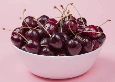 White bowl of fresh red cherries on a pink background. close-up