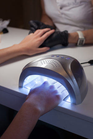Girl dries nail Polish in a UV lamp in a beauty salon.の写真素材