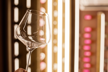 The empty glass on the background of illuminated shelves with bottles of wine.の写真素材