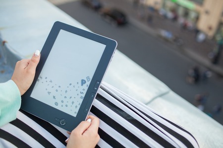 Close up of female hands with manicure hold an e-book. Girl reading a book on the roof of the...