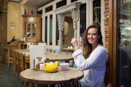 Attractive and lonely girl sitting in a cafe, drinking tea from the yellow teapot.の写真素材
