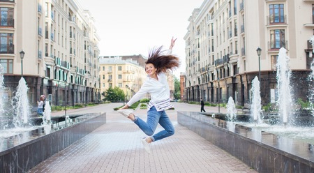 Young sporty girl jumping for joy at the fountain in the residential complex. Female in flight with...