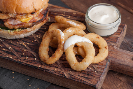 Close up of fried onion rings on the Board, with a white garlic sauce on wooden background.の写真素材