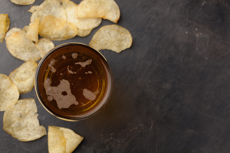 Close-up old beer in a long glass and of potato chips on a dark stone with copy space. Top view.の写真素材