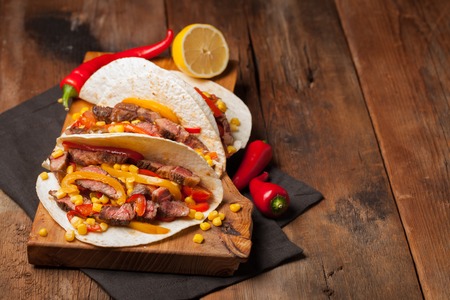 Three Mexican tacos with marbled beef, black Angus and vegetables on old rustic table. Mexican dish with sauces guacamole and salsa in bowls. copy space.の写真素材