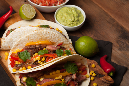 Three Mexican tacos with marbled beef, black Angus and vegetables on old rustic table. Mexican dish with sauces guacamole and salsa in bowls.の写真素材