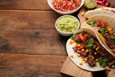 Three Mexican tacos with marbled beef, black Angus and vegetables on old rustic table. Mexican dish with sauces guacamole and salsa in bowls. Top view with copy space.の写真素材