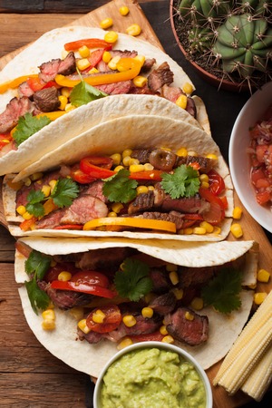 Three Mexican tacos with marbled beef, black Angus and vegetables on old rustic table. Mexican dish with sauces guacamole and salsa in bowls. top view.の写真素材