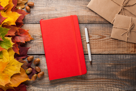 Red notebook with pen and paper envelopes on old wooden table. Mixed maple autumn leaves and acorns next to a closed notebook.の写真素材