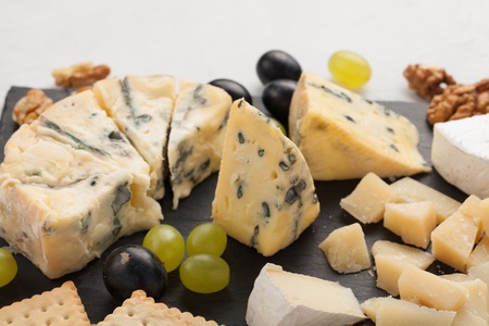 Assorted cheeses with white grapes, walnuts, crackers and on a stone Board. Food for a romantic date on a light background.の写真素材
