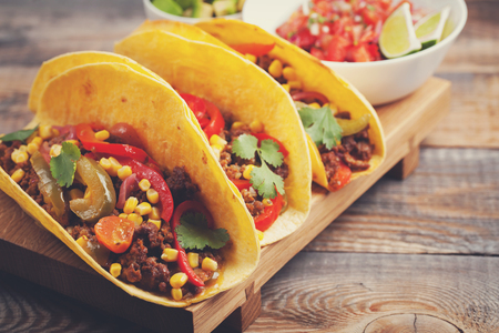 Three Mexican tacos with minced beef and mix vegetables on old rustic table. Mexican dish with sauce salsa in bowl and avocado. Spicy and hot street food. Close-upの写真素材