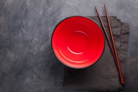 Empty red glass bowl of Chinese noodles and wooden sticks on dark concrete background. Top view with copy space. Flat lay.の写真素材