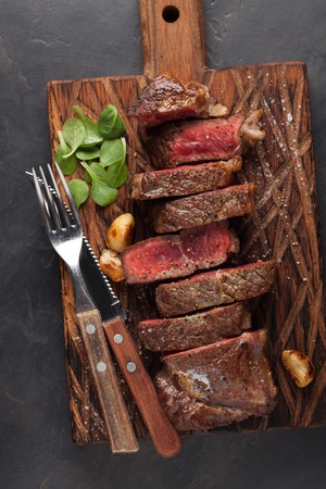Closeup ready to eat steak new York beef breeds of black Angus with herbs, garlic and butter on a wooden Board. The finished dish for dinner on a dark stone background. Top view.の写真素材