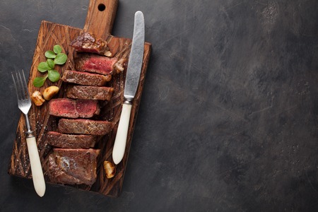 Closeup ready to eat steak new York beef breeds of black Angus with herbs, garlic and butter on a wooden Board. The finished dish for dinner on a dark stone background. Top view with copy space.の写真素材