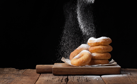 Baker sprinkles sweet donuts with powder sugar on black background. Delicious, but unhealthy food on the old wooden table with copy space.の写真素材