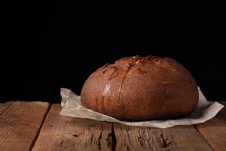 Tasty rustic bread on wooden table on black background with copy space for text.