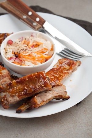 Grilled pork ribs in barbecue sauce and honey with sauerkraut on white plate. Snack to beer on a light stone tableの写真素材