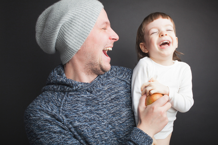 Dad plays with a lovely little son, sitting on his hands on a black background in the studio. It amuses it with Apple and they both laugh. Photos to celebrate father's day.の写真素材