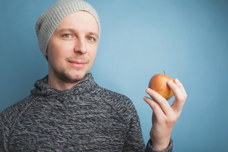 The guy in the hat holding an Apple in hand against a blue background.の写真素材