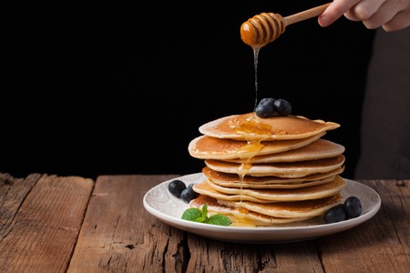 The chef pours honey pancake stack with blueberries and mint on black background. Copy space for your text.の写真素材