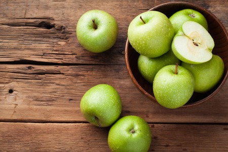 Ripe green apples in a wooden bowl on an old rustic table. Useful fruits on wooden background. Top view with copy space.の写真素材
