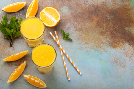 Two glasses with freshly squeezed orange juice and mint on an old rusty blue background. Top view with copy space.の写真素材