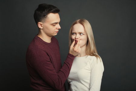 Portrait of a beautiful young couple in love posing at studio over dark background. The guy makes his girlfriend duck face.の写真素材