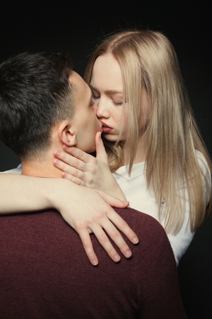 Portrait of a beautiful young couple in love posing at studio over dark background. Guy and girl kissing close up.の写真素材