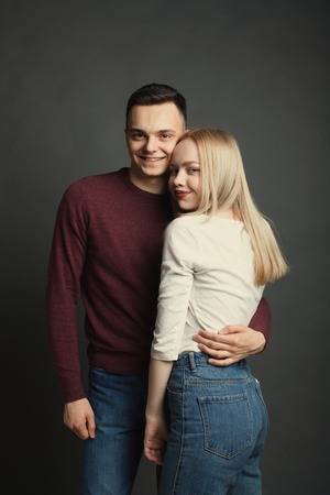 Portrait of a beautiful young couple in love posing at studio over dark backgroundの写真素材